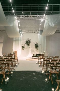 an indoor wedding setup with white draping and candles on the aisle for guests to sit down