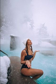 a woman in a bathing suit sitting on the edge of a hot tub with snow around her