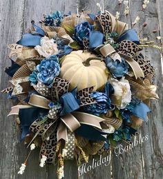 a wreath with blue flowers and leopard print ribbon on top of a wooden table next to an orange pumpkin