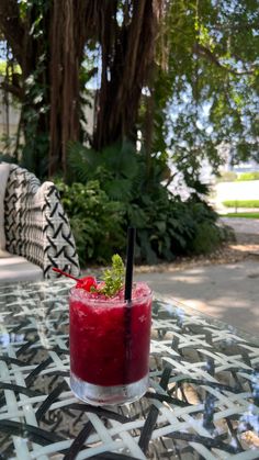 a red drink sitting on top of a glass table next to a green leafy tree