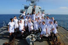 a group of people standing on the deck of a ship posing for a photo with their arms in the air