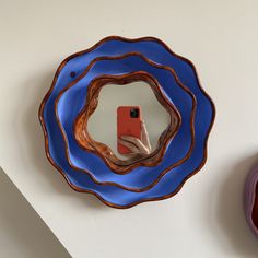 a hand holding a cell phone in front of a blue plate with a mirror on it