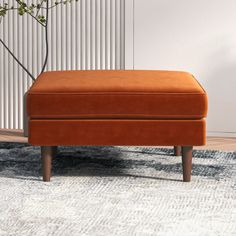 an orange footstool sitting on top of a rug in front of a white wall