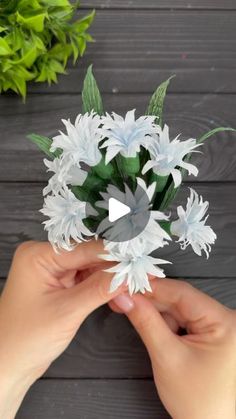 someone is holding some white flowers in their hands and making a flower arrangement with paper