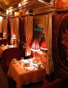 a dining car on a train with red and gold decor, including two tables covered in white tablecloths