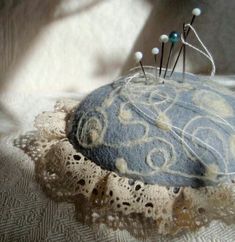 a pin cushion sitting on top of a white lace covered table cloth with pins sticking out of it