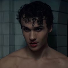 a shirtless young man with dark hair and no shirt standing in front of a white brick wall