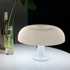 a white table with a vase and bottle on it next to a lamp that has a flower in it