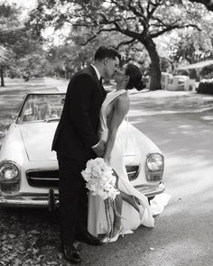 a bride and groom kissing in front of a classic car