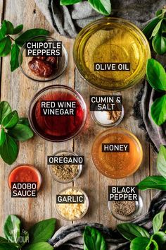 different types of vinegars and seasonings in glass bowls on a wooden table surrounded by green leaves