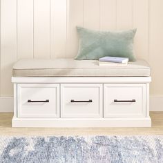 a white bench with two drawers and a blue pillow on it in front of a wall