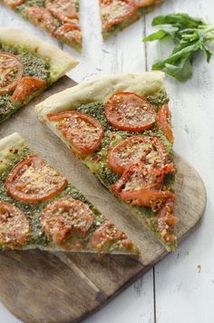 slices of pesto pizza on a wooden cutting board with basil and tomato toppings