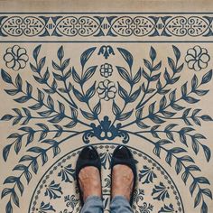 a person standing in front of a blue and white tile design on the floor with their feet propped up