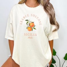 Featuring a retro orange fruit design, the Aranci Di Sicila T Shirt is perfect for any occasion. The shirt's unique design evokes a vintage Italian aesthetic that is comfortable and stylish. Whether you're a foodie or you're simply a lover of all things Italy, this cozy tee is a must-have addition to your wardrobe. Give it as a gift to someone special your life or treat yourself to this unique and timeless piece. * PRODUCT DETAILS * ♥ Double needle stitching on all seams. The garment is sewn aro Casual Orange Fruit Print Top, Retro Orange T-shirt For Spring, Casual Peach Tops With Letter Print, Orange Top With Letter Print And Relaxed Fit, Orange Relaxed Fit Top With Letter Print, Relaxed Fit Orange Top With Letter Print, Vintage Fruit Print Crew Neck Tops, Vintage Crew Neck Tops With Fruit Print, Orange Graphic Print Top With Relaxed Fit