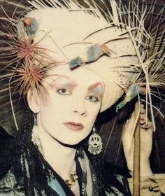 a woman with feathers on her head is holding an umbrella and looking at the camera