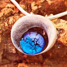 a silver pendant with blue and red glass in it on some rocks or dirt area