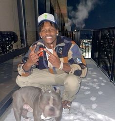 a man kneeling down next to a dog on top of snow covered ground with buildings in the background