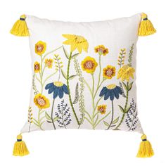 a white pillow with yellow flowers and blue daisies on the front, along with tassels