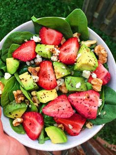 a white bowl filled with spinach, strawberries and avocado