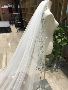 a white veil with flowers on it sitting on top of a mannequin's head