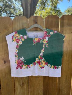 a green and white shirt hanging on a wooden fence next to a tree in the background