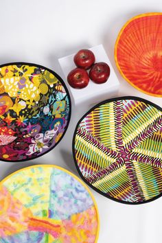 four colorful plates with designs on them next to apples