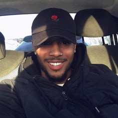 a man sitting in the back seat of a car wearing a hat and smiling at the camera