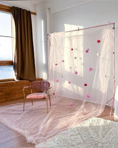 a chair sitting in front of a white curtain with pink flowers on it and a window behind it