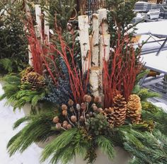 a planter filled with pine cones and evergreens next to snow covered benches in the background