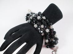 "A spectacular beaded bracelet.  Constructed in six rows of faceted black glass beads with clear rhinestone ball accents, the bracelet is wide, dramatic and oh-so-glamorous.  It's unsigned, most likely dates to the 1980s, with superb quality wiring holding the beads in place.  It's in excellent vintage condition ready to accessorize in 2024! Length 10\" (to accommodate the rows of beads.  Fits my 6.5\" wrist with some room) Width 2\"" Black Faceted Beads Crystal Bracelet For Party, Black Crystal Bracelet With Faceted Beads For Party, Party Multi-strand Faceted Beaded Bracelets, Black Crystal Bracelet With Round Beads For Party, Black Beads Crystal Bracelet For Party, Black Beaded Crystal Bracelet For Party, Party Crystal Bracelet With Black Beads, Faceted Beaded Bracelets For Party With Round Beads, Black Crystal Bracelet For Party