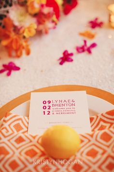 an orange and white plate with a yellow lemon on it next to a table cloth