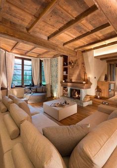 a living room with couches and a fire place in the center, surrounded by wooden beams