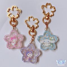 three key chains with hello kitty charms hanging from them on a white surface, one is gold and the other is pink