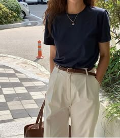 a woman is standing on the sidewalk with her hand in her pocket and holding a brown bag