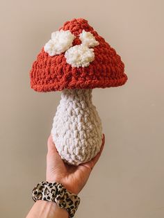 a hand holding up a crocheted mushroom with white and red flowers on it