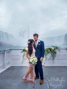 a bride and groom standing on the deck of a boat in front of waterfalls