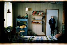 a person standing in a room with a bed and book shelf on the wall next to it