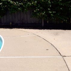 an empty swimming pool in the middle of a backyard with fence and trees behind it