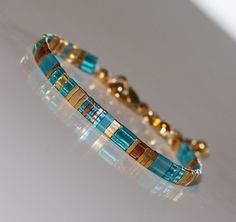 Tila Bracelet in transparent aqua with 24kt golden accents - Miyuki tila beads - Bohemian summer vibes - Glass beads Add a touch of summer to your jewelry collection with this stunning Tila bracelet featuring glass tile beads in aqua and 24kt gold. Handcrafted with Japanese Miyuki glass beads, this piece exudes boho chic vibes and is the perfect accessory for any summer outfit. Finished with a durable stainless steel lobster clasp and extension chain, this piece is not only stylish but also prac Sea Glass Crafts Jewellery, Tila Bracelets, Tila Beads, Bracelets Handmade Diy, Dainty Bracelet, Aqua Turquoise, Handmade Jewelry Gift, Bracelet Beaded, Dainty Bracelets