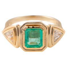 an emerald and diamond ring with three diamonds on the sides, set in yellow gold