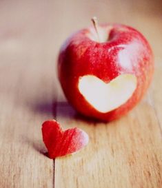 an apple with a heart cut out of it sitting on a wooden table next to another apple