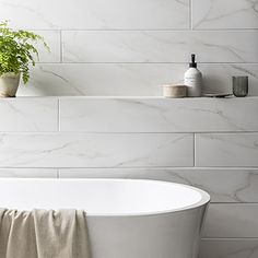 a white bath tub sitting in a bathroom next to a shelf with a plant on it