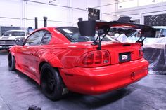 a red car parked in a garage next to another car with its hood up on