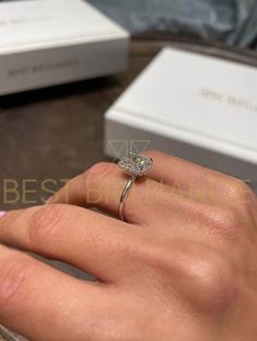 a woman's hand with a diamond ring on top of her finger next to two boxes