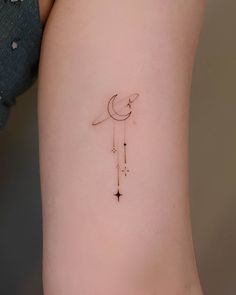 a small tattoo on the side of a woman's thigh with a crescent and stars hanging from it