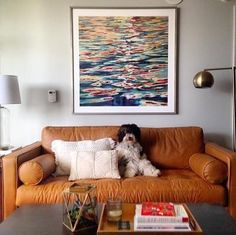 a dog sitting on top of a brown couch next to a coffee table and lamp