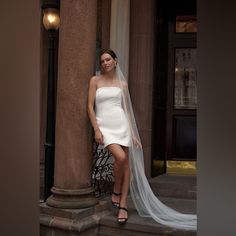 a woman in a short white dress leaning against a pillar with her veil pulled back