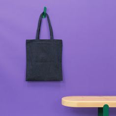 a black tote bag hanging on a purple wall next to a wooden table and bench