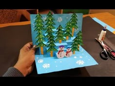 someone is making an origami christmas card with snowmen and trees on it