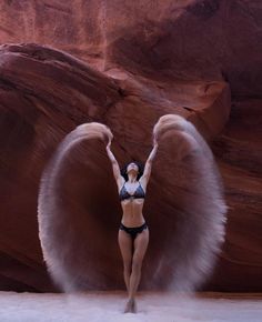 a woman with angel wings standing in front of a rock formation and posing for the camera